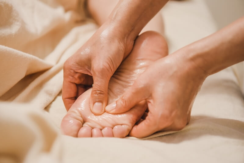 Das Bild zeigt eine Nahaufnahme von einer Reflexzonenmassage mit zwei Händen an einem Fuß.