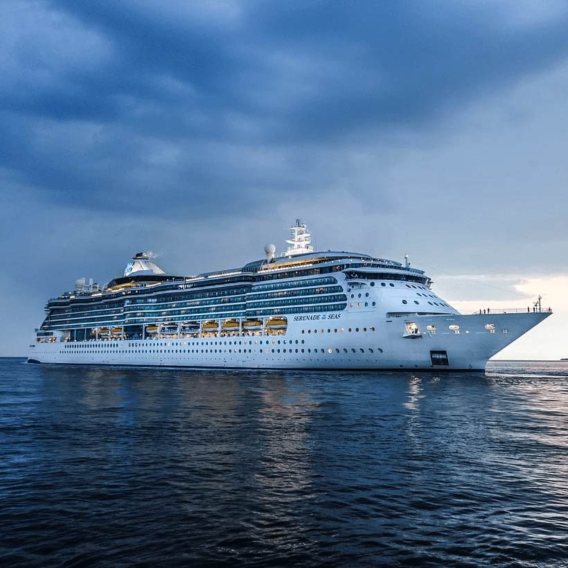 Ein großes Kreuzfahrtschiff auf ruhigem Wasser bei bewölktem Himmel, mit dem Namen Serenade of the Seas sichtbar.